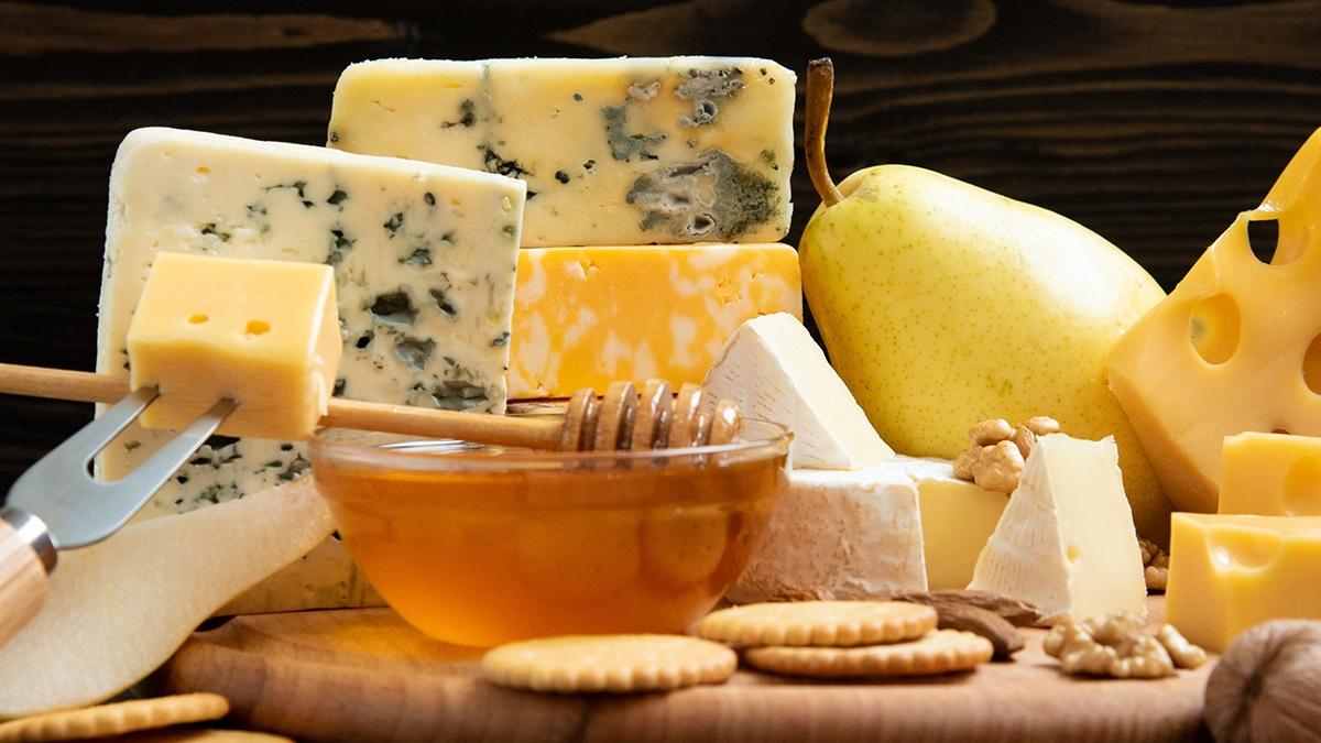 Delicious cheese on the table. Various types of cheese on a rustic wooden table. Assortment of cheeses with nuts, fruits and honey.