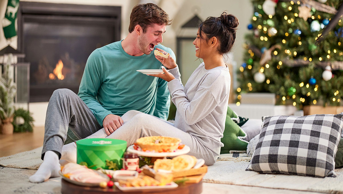 Couple eating food in front of a Christmas tree.