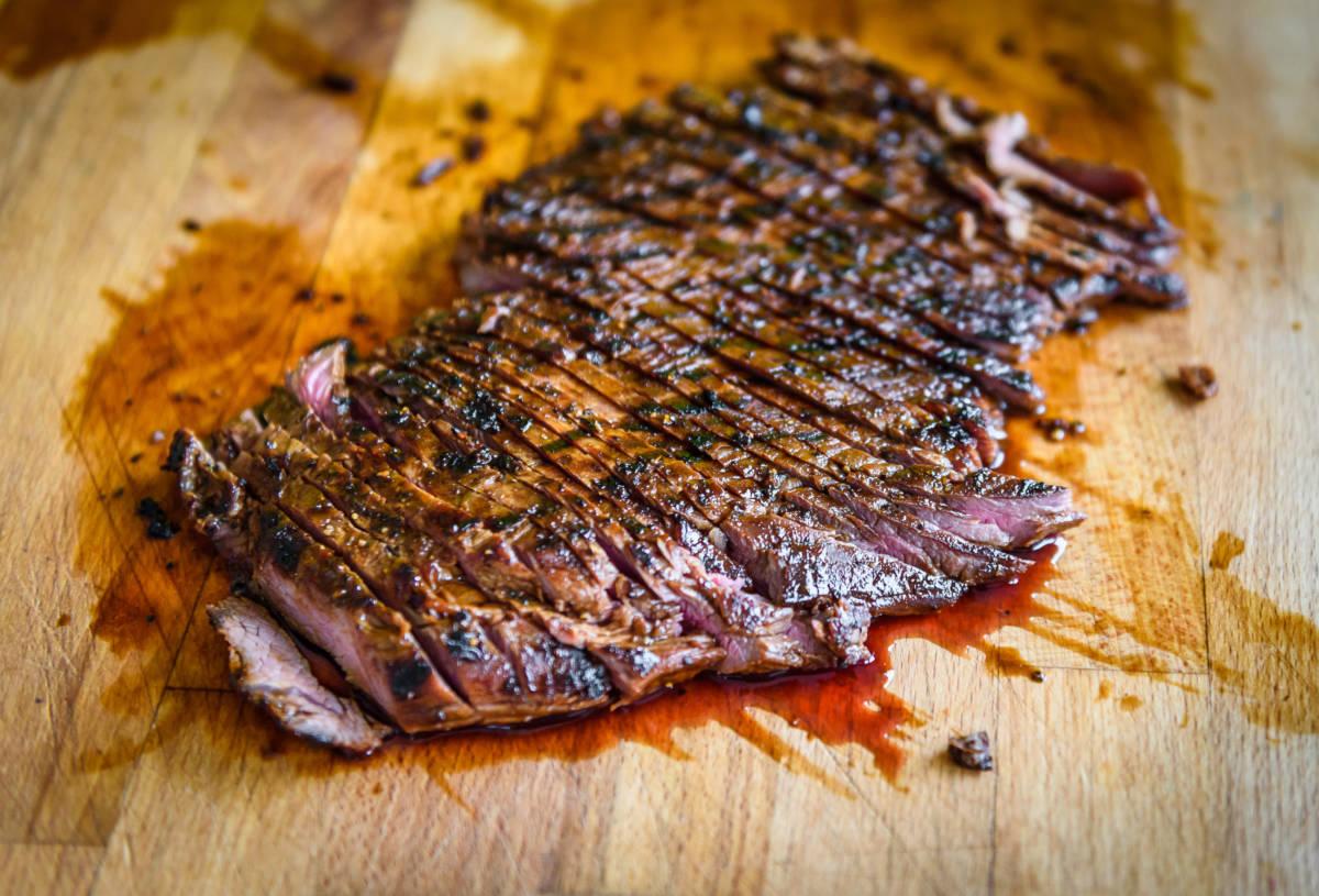 Sliced grilled juicy marinated angus beef flank steak on wooden board. Finished juicy medium rare meat is sliced and ready for serving. Professional gourmet restaurant style steak.