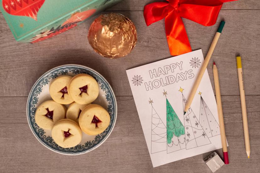A photo of holiday spirit with a plate of Christmas cookies next to a half colored in picture of Christmas trees with pears sitting next to the picture.