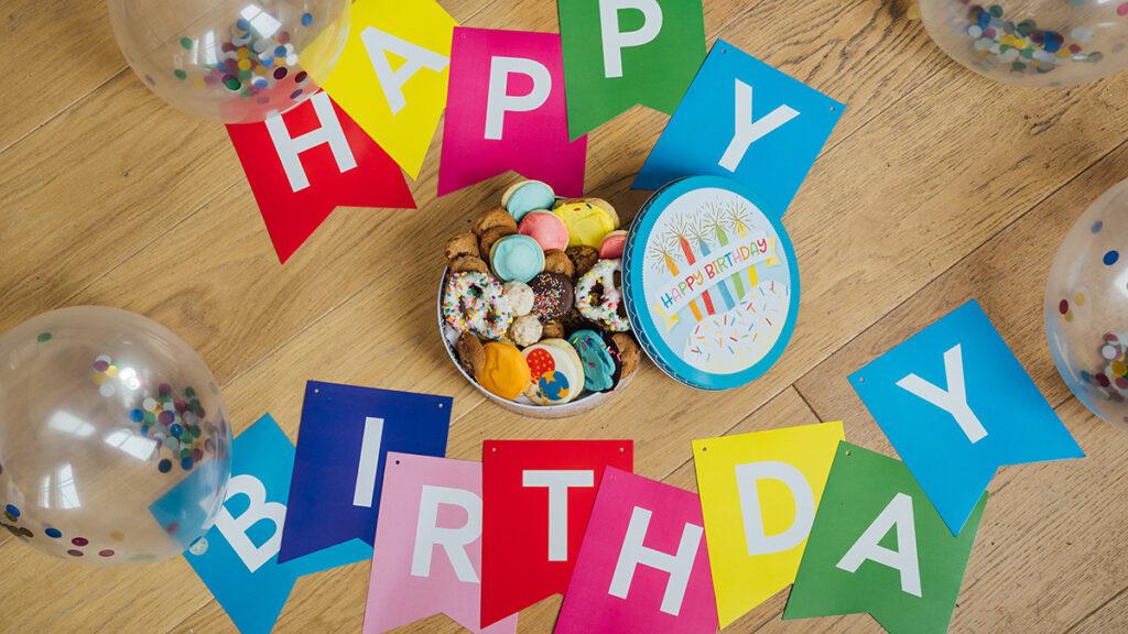 Birthday traditions around the world image   happy birthday banner on a table surrounding a tin of cookies