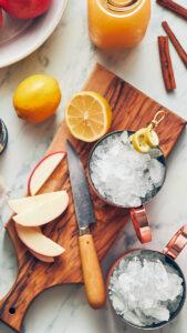 Moscow mule recipe image   cups filled with ice on a cutting board with chopped apples and lemons