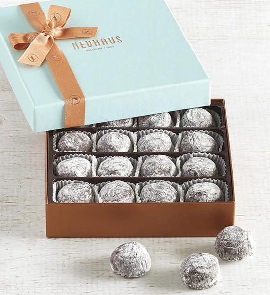 anniversary gift guide image   champagne truffles in a gold and blue box with three truffles sitting outside of it.