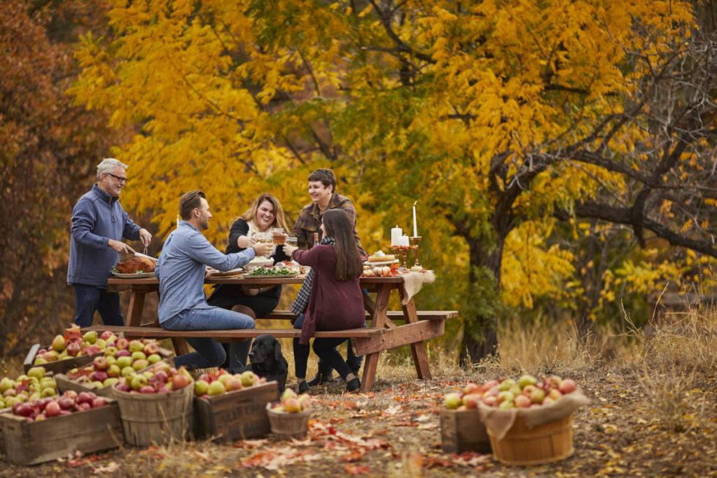 fall leaves image   group of people having dinner outside surrounded by fall leaves and barrels of apples
