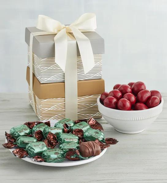 Gifts under $ for Christmas with two gift boxes stacked on top of each other next to a bowl of chocolate covered cherries and a plate of chocolates wrapped in foil.
