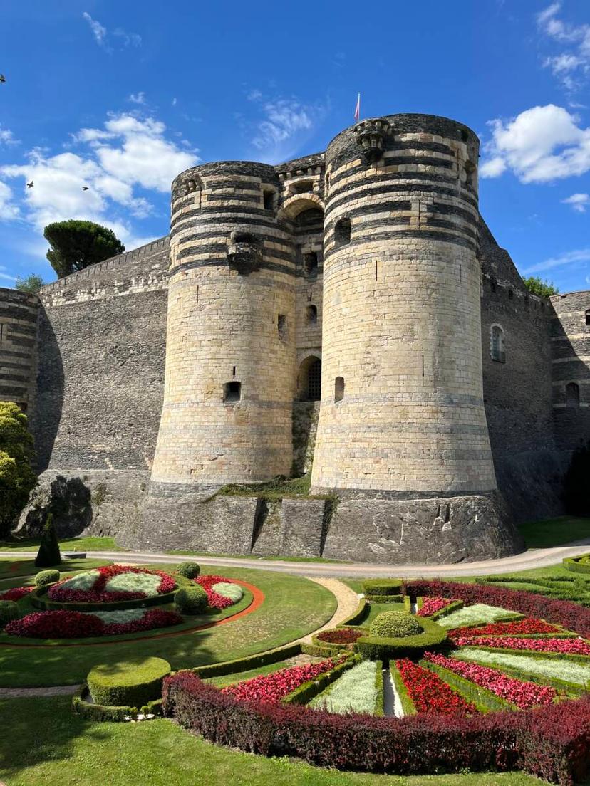A view of the Chateau d'Angers, and two of its  towers made of slate and limestone, overlooking the manicured gardens.