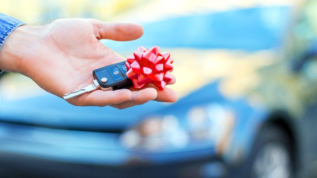 Unique birthday gift ideas with a hand holding a car key with a bow on top of it.