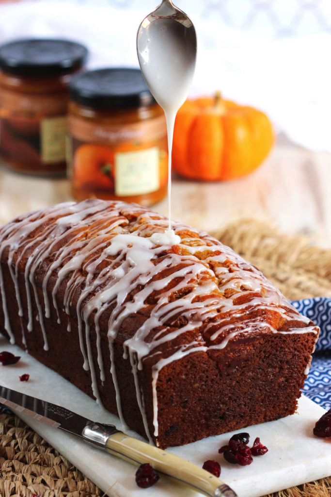 Loaf of pumpkin bread with a spoon drizzling white glaze over it.