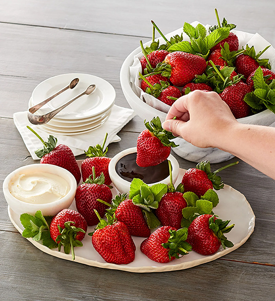 Mothers Day gift ideas with two plates of strawberries and a hand dipping a strawberry in a bowl of chocolate sauce