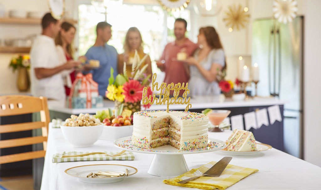 A photo of January birthdays with a cake on a table and a group of people in the background.