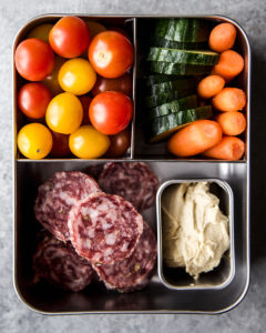 Road trip snack box with vegetables, hummus, and salami.