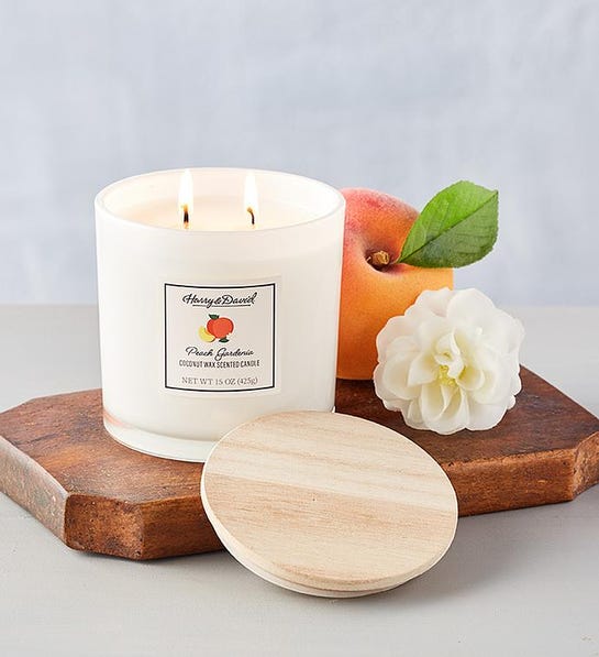 A photo of birthday gift ideas with a burning candle on a wooden board with a peach and a flower next to it