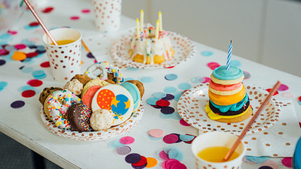 Birthday tradition image   birthday cake and cookies with candles on confetti covered table.