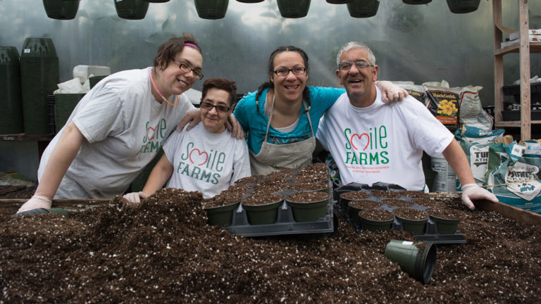 Smile farms image group posing for photo in front of dirt