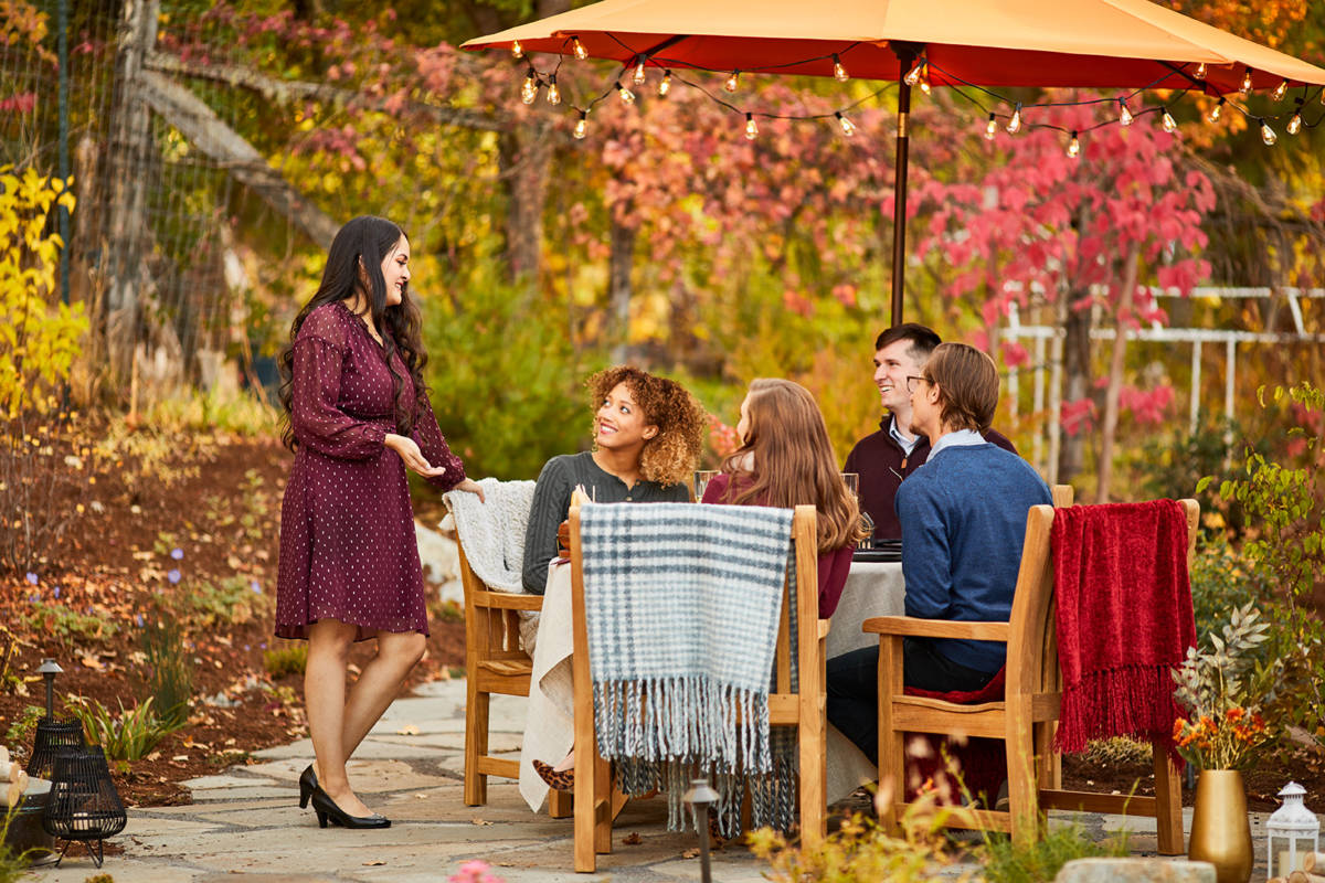 October birthday image   group of people sitting outside at a table with fall leaves in the background