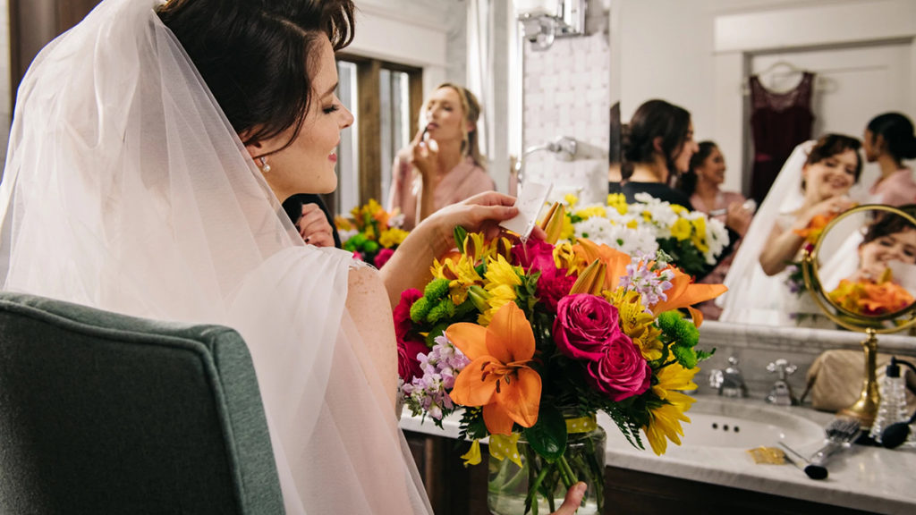 history of marriage with a bride looking at her photos while bridesmaids do their makeup in the background