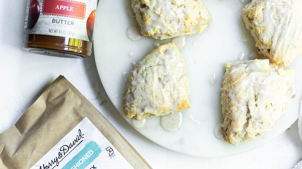 A photo of apple pie scone recipe with a bag of scone mix and a jar of apple butter next to a plate of scones