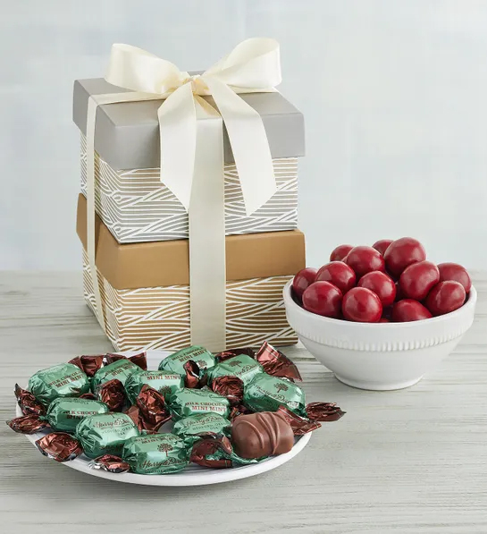 Gifts under  for Christmas with two gift boxes stacked on top of each other next to a bowl of chocolate covered cherries and a plate of chocolates wrapped in foil