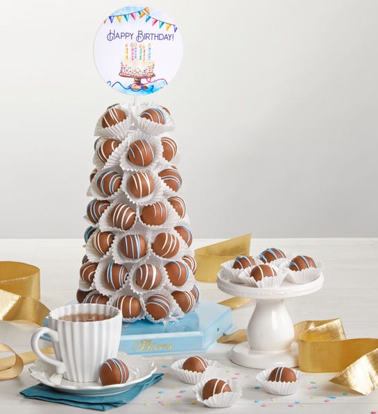 A photo of birthday gift ideas with a tower of truffles next to a plate of the same truffles and a mug of hot chocolate