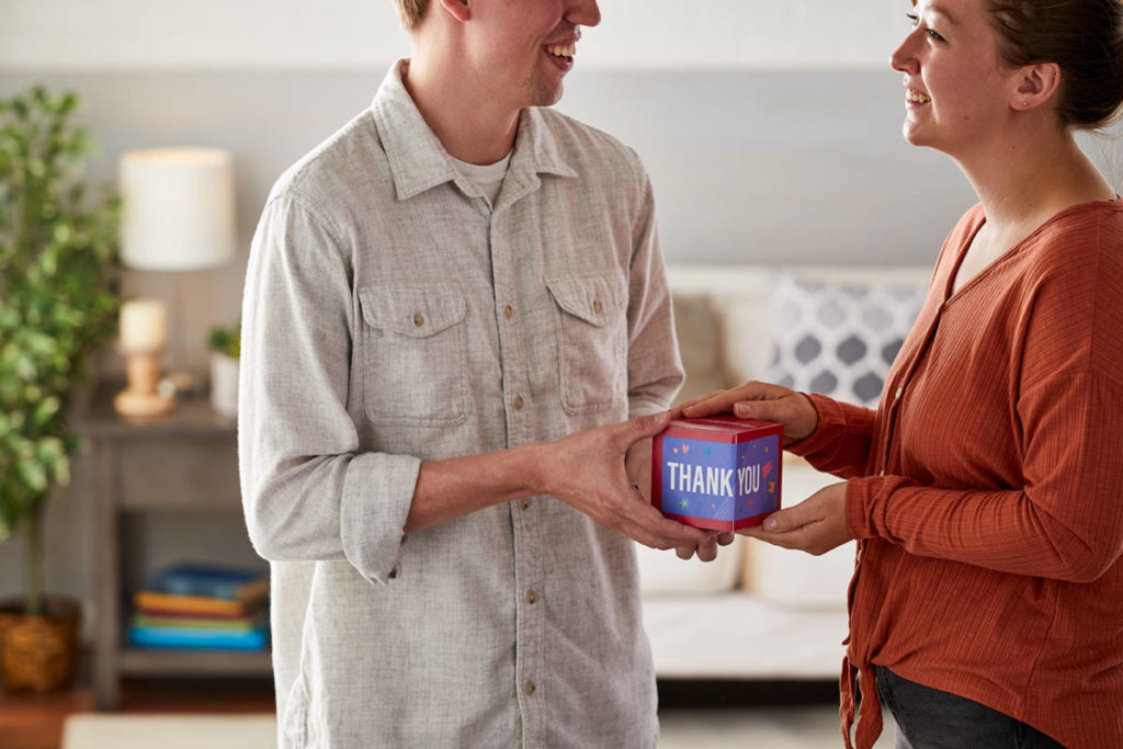 A photo of what to write in a thank you card with a man giving a woman a gift.