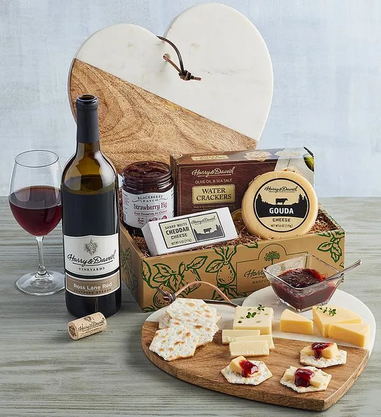 Gifts for couples with a box full of cheese crackers and a heart shaped cheese board next to a bottle of wine