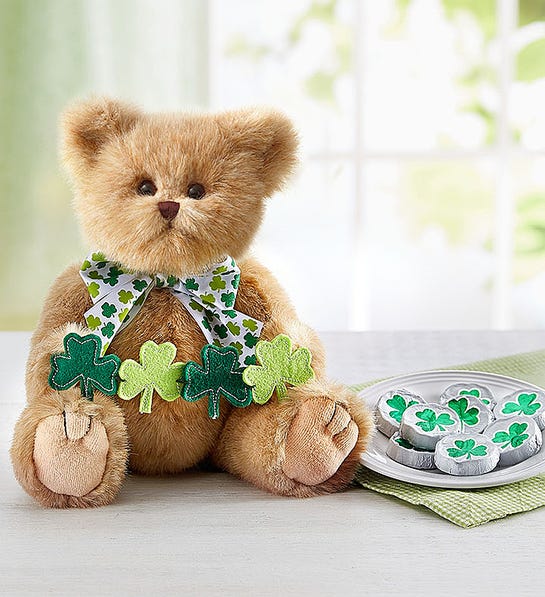 A photo of St Patricks Day with a stuffed bear holding a garland of shamrocks sitting next to a plate of chocolates wrapped in tinfoil