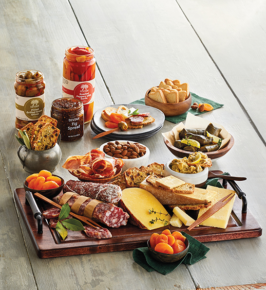 A photo of gifts for women with an array of cheese meat and crackers on a board with the same ingredients sitting in bowls and jars next to it