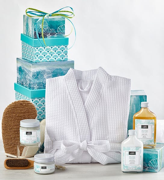 A photo of gifts for women with a stack of blue boxes behind a folded bathrobe and several bottles of lotion and other spa amenities