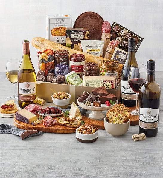 A photo of gifts for women with a box full of chocolate meat crackers bread cheese spreads and other snacks with the same ingredients and three bottles of wine surround the box