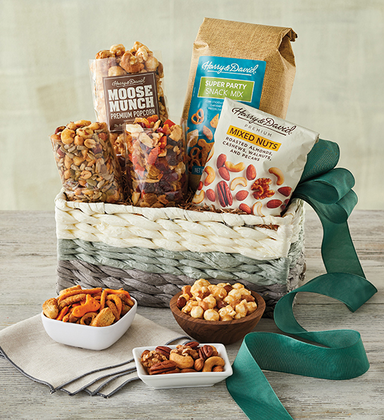 A photo of gifts for men with a basket full of mixed nuts caramel corn and other snacks with the same ingredients in three bowls in front of the basket