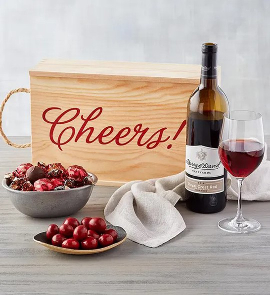 A photo of a picnic with a wooden box that says cheers next to a bottle of wine and several bowls of chocolate