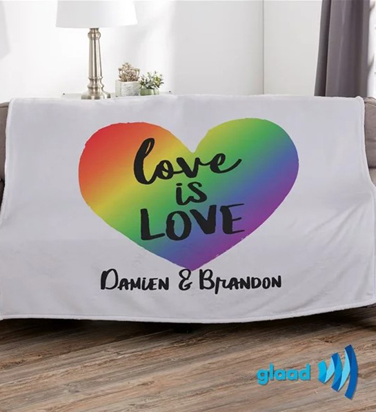 A photo of pride month gifts with a personalized blanket with a rainbow heart with the words love is love inside it