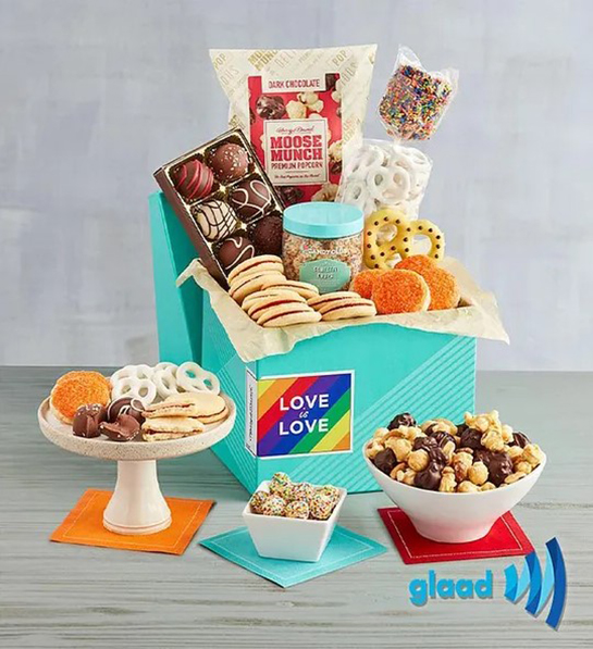 A photo of pride month gifts with a box full of chocolate cookies popcorn and other treats surrounded by the same items