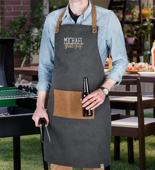 Photo of grilling gifts with a person wearing a personalized apron and holding tongs in one hand and a beer in the other