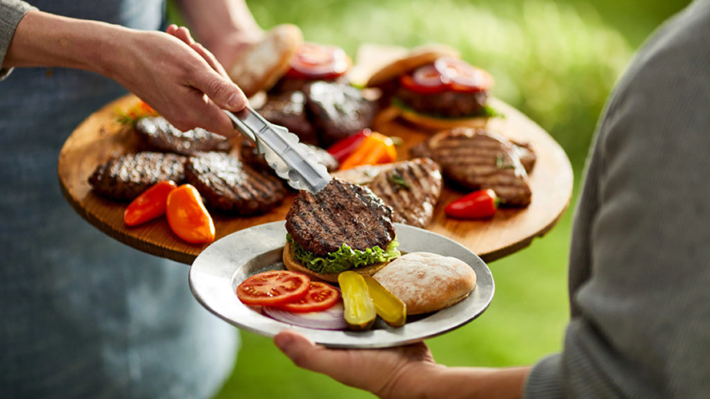 Photo of how to grill with someone placing a burger on someone else's plate.