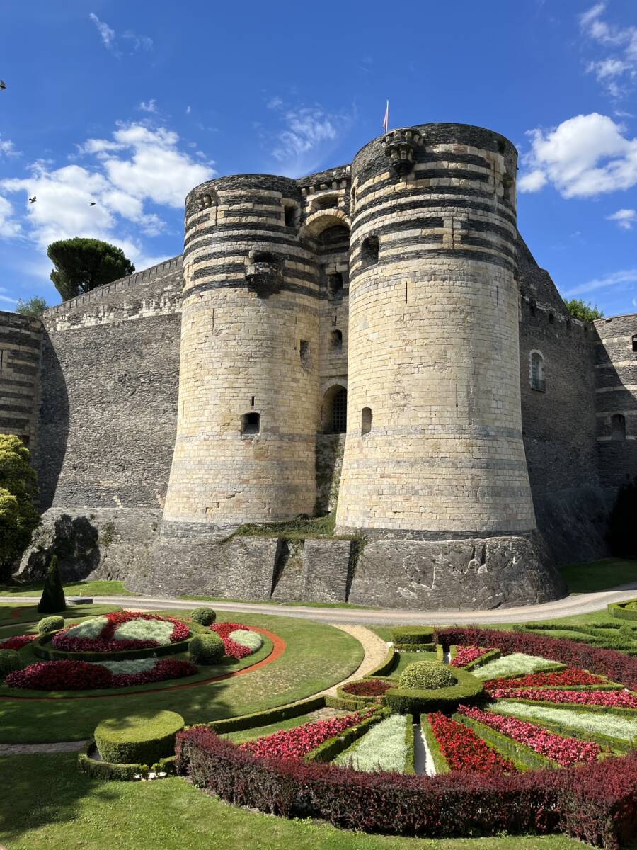 A view of the Chateau d'Angers, and two of its towers made of slate and limestone, overlooking the manicured gardens.