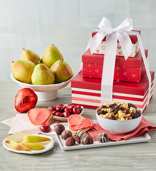 Valentines Day gifts for her with a stack of red gift boxes tied with a bow surrounded by fruit chocolate and cookies