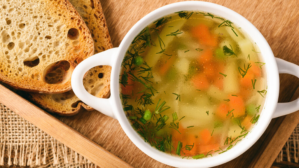 Chicken soup in a bowl with slices of bread next to it.