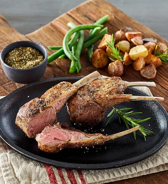 Double cut lamb chops on a black plate with veggies and dipping sauce