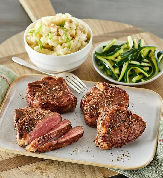 Lamb porterhouse chops on a plate next to veggie side dishes