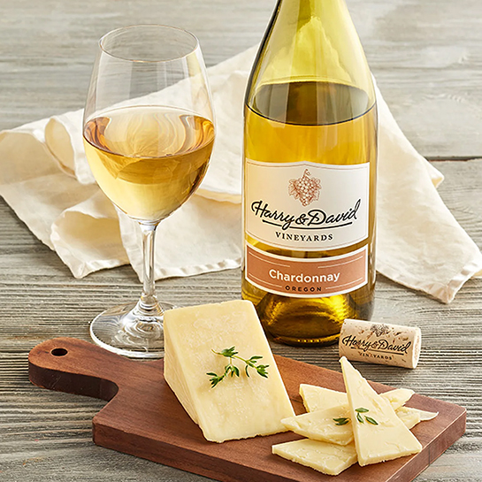 Bottle of chardonnay next to a glass of wine and a cutting board with slices of cheese