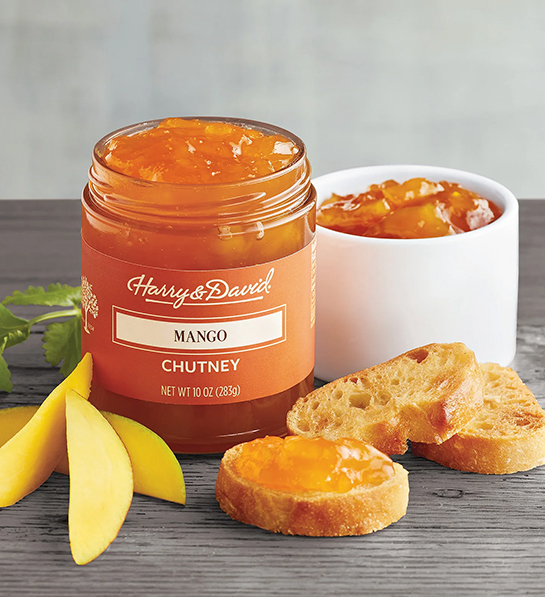 Jar of mango chutney next to a bowl of the same chutney surrounded by slices of mango and bread