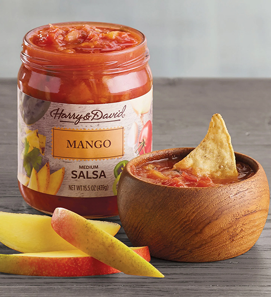 Medium mango salsa in a jar next to a bowl of salsa and slices of mango