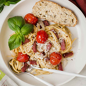 Tomatoes and salami in a pasta dish with a slice of bread