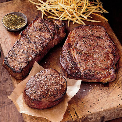 Several cuts of cooked steak on a wooden cutting board with French fries and rub